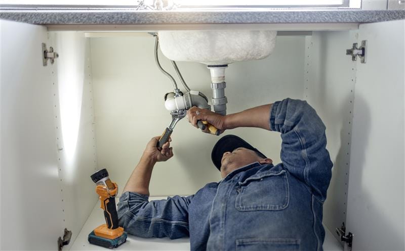 Plumber repairing pipes beneath a bathroom sink in Imperial Beach