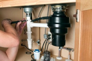 Plumber repairing a garbage disposal beneath a kitchen sink in Imperial Beach