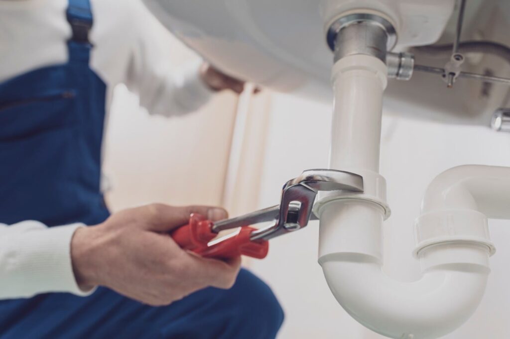 Plumber repairing a white drain pipe beneath a sink in Imperial Beach