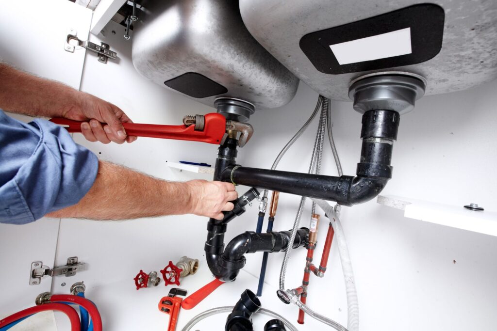 Plumber repairing drain pipes beneath a kitchen sink in Imperial Beach